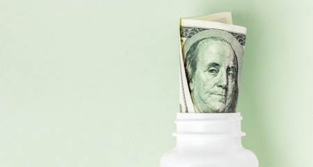 Roll of money Bills in white pill bottle on pink background with copy space. medicine flat lay