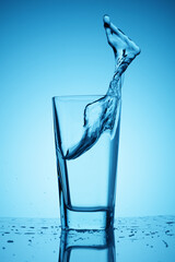 Splashes of clean drinking and fresh water in a glass cup on a classic blue background