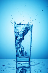 Beautiful splashes in a glass glass with clean drinking water on a classic blue background