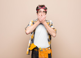 young housekeeper man covering mouth with hands with a shocked, surprised expression, keeping a...