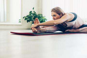 Naklejka premium Young woman doing stretching exercise by mirror in bright yoga class room
