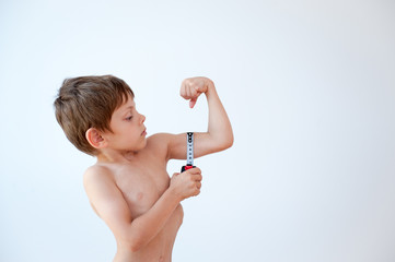 funny healthy little caucasian boy measuring his strong muscle using tape on white backgroun with...