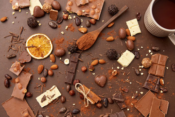 sweets, confectionery and food concept - hot chocolate with nuts, candies, cinnamon and cocoa powder on brown background