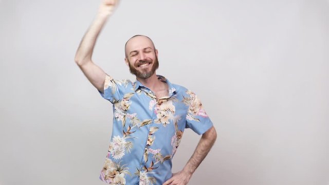 Happy bearded bald man dancing and having fun on white background. Cheerful tourist wearing hawaiian shirt smiling.