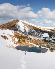 Amazing landscape with lake in spring snowy mountains. Hiker with backpack coming down in the snow