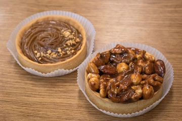 Brown round tartlets on wooden background. Two tarts with caramel and peanuts.