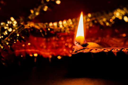 glowing terracotta lamp with golden and red chunni in the background. diwali concept