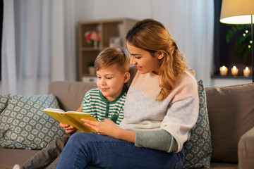 family, leisure and people concept - happy smiling mother and little son reading book sitting on sofa at home