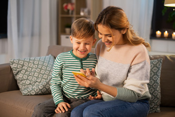 family, technology and people concept - happy smiling mother and little son sitting on sofa and...