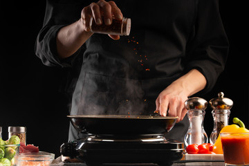 The chef fries the meat in a pan, sprinkles with seasoning. Freezes in motion. Delicious and healthy food. Vegetables and meat. Restaurant and hotel business, recipe book