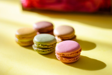 Colorful macaroons on a yellow background, aligned and illuminated by the sun's rays, selective focus