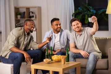 friendship, leisure and people concept - male friends with smartphone taking selfie and drinking beer at home at night