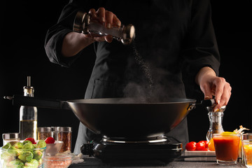 The chef fry the meat in a pan, sprinkling with salt, freezing in motion. Against the background of vegetables. Culinary recipes, tasty food.