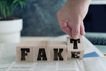 FAKE or FAKT, German for fact, on wooden blocks on newspaper, real news or fake news concept