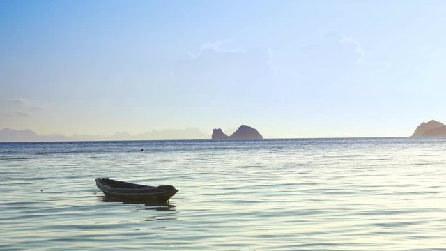 A wooden boat sways on the waves of the ocean near the shore. Big rock in the water on background. Tropical island Romance by the ocean. Tropical landscape