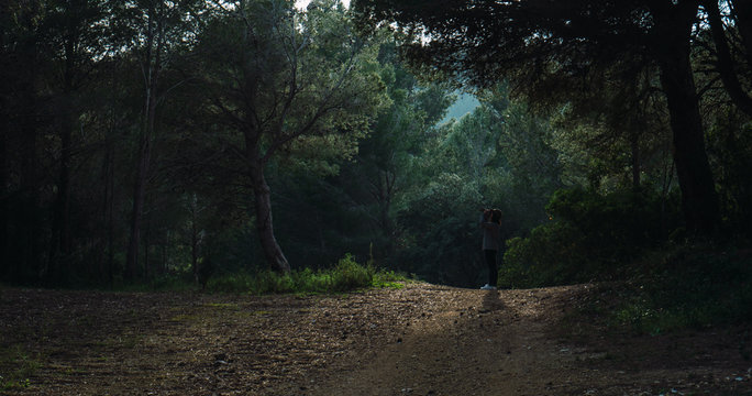 A young girl taking pictures with an analog camera in the dense green forest