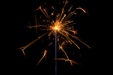Sparkler with lots of sparks burning bright isolated on black background.