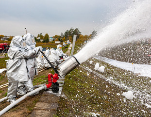 Firefighters in high-temperature protective suits in exercises extinguish foam