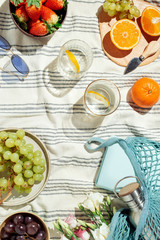 Feminine summer picnic flatlay, fruits, berries and lemon water on striped cotton blanket