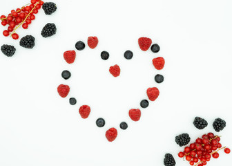View from above of raspberries, blueberries in the shape of a heart, with blackberries and gooseberries in the corners. Space in the center for text. Healthy food concept.