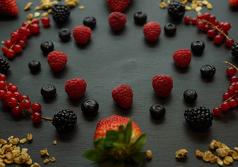 Close up view of strawberries, blackberries, blueberries, raspberries, currants and granola on a black slate background. Healthy food concept.