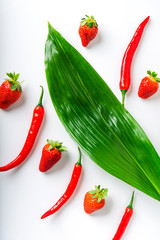 red chili peppers and ripe strawberries and green leaves on a white background