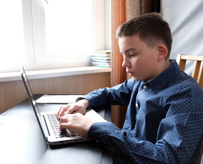 man works on a laptop at a table in front of a window. back light