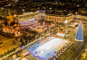Fototapeta na wymiar New Year's center of the city of Tula in Russia. An ice rink, a decorated Christmas tree and beautiful buildings with lighting in the central square, a view from above. Aerial photography