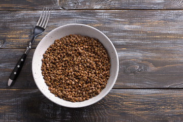 Bowl of boiled red unpolished lentils in a ceramic bowl on a wooden table
