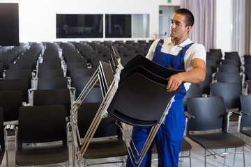 Worker carrying chairs in empty room