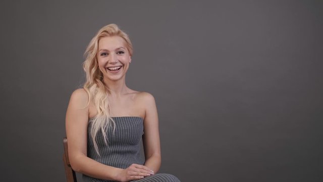 A woman is smiling and talking to the camera. Beautiful girl on television. The blonde gives an interview indoors in the studio on a gray background