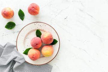 Summer lunch. Red peaches on white background with tablecloth and leaves top-down copy space