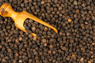 Spice background, Background made of many whole black peppercorns and a spice shovel made of olive wood, close up, top view