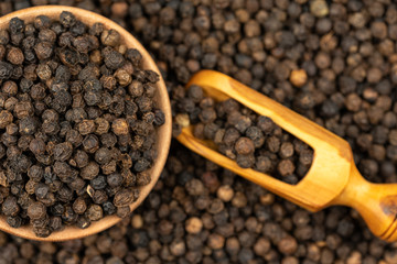 Spice background, Background made of many whole black peppercorns and a wooden bowl also filled with peppercorns and a spice shovel, close up, top view