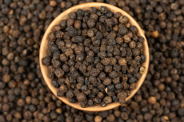Spice background, Background made of many whole black peppercorns and a wooden bowl filled with peppercorns, close up, top view