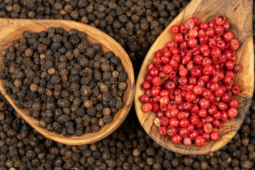 Spice background, Background made of many whole black peppercorns and two cooking spoon made of olive wood also filled with black and red peppercorns , extreme close up, top view