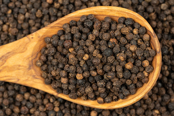 Spice background, Background made of many whole black peppercorns and a cooking spoon made of olive...