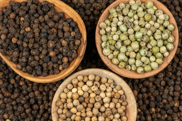 Spice background, Background made of many whole black peppercorns and a cooking spoon made of olive wood and two wooden bowls filled with black, green and white peppercorns , extreme close up