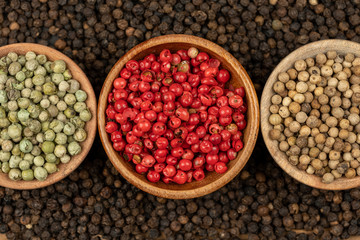 Spice background, Background made of many whole black peppercorns and three wooden bowls also filled with white, green and red peppercorns , extreme close up, top view