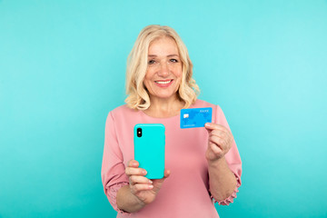 Fototapeta premium Happy woman in the pink dress holding credit card with mobile