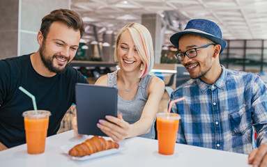 Cheerful diverse friends using tablet during lunch in cafe