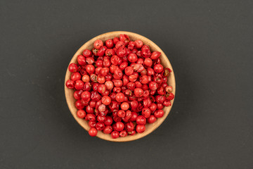 A small wooden bowl filled with red peppercorns on a black background, close up, top view