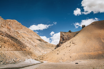 Picturesque mountain landscape on the endless Leh - Manali road. Blue sky with white clouds and desert lifeless rocky mountains. Distant travel destinations concept image.