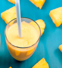 fresh pineapple juice in a glass with a straw on a blue and green background