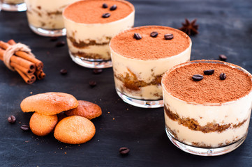 classical tiramisu dessert in a glass sprinkled with cocoa and decorated with coffee beans on a dark background, luxury dessert