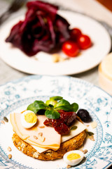 A rusk with cheese, turkey breast, quail egg, sun-dried tomato and valerianella locusta
