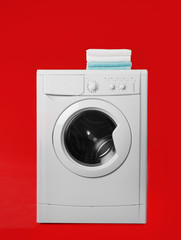 Modern washing machine with stack of towels on red background. Laundry day