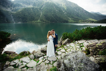 bride with beautiful white dress and bride overlooking beautiful green mountains and lake with blue water