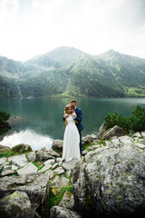 bride with beautiful white dress and bride overlooking beautiful green mountains and lake with blue water