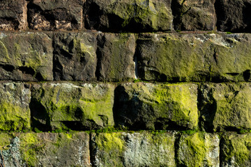 Mauer Bruchstein alt Moos Algen Pflanzen grün Sonnenlicht Schatten Struktur Hintergrund Vintage Gebäude Sockel Fundament Handwerk